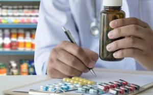 دست فردی که شیشه دارو است و چندتا قرص جلوش است و در حال نوشتن است